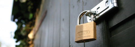 Abus brass padlock attached through a hasp & staple on a black wooden fence